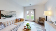 Located at 5945 Arlo Way in Indianapolis, IN, this well-designed one-bedroom, one-bathroom home offers a clean, modern aesthetic throughout its single-floor layout. Light wood-style flooring flows through the main living areas, complemented by crisp white walls and recessed lighting that create a bright, airy atmosphere.

The living room is a welcoming focal point, featuring French doors that open to a lush green outdoor view, allowing natural light to fill the space. A dedicated area for a sideboard and artwork adds a refined, curated touch to the room's character.

The kitchen is thoughtfully appointed with white shaker cabinetry, light quartz countertops, a peninsula with a sink, and a full suite of stainless steel appliances including a refrigerator, electric range, and microwave. Recessed lighting enhances the clean, functional design.

The spacious bedroom features plush carpeting, a large window overlooking a green outdoor setting, and ample wall space for artwork. An adjacent closet provides generous storage. The hallway features built-in double-door closets and a decorative round mirror, adding both practicality and style.

The bathroom offers a glass-enclosed walk-in shower with tile surround and built-in open shelving for organized storage. Every detail reflects a cohesive, modern design sensibility.