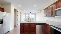 Located at 6743 W 135th St in Overland Park, Kansas, this well-appointed single-floor residence offers three bedrooms, four bathrooms, and a thoughtfully designed layout. The open kitchen and living area serve as the heart of the home, featuring rich cherry-toned cabinetry, granite countertops, wood-look tile flooring, and a full suite of stainless steel appliances including a refrigerator with ice maker, electric range, over-the-range microwave, and dishwasher. A central island with a dual basin sink adds both function and visual appeal. Crown molding and recessed lighting lend a polished finish to the space. The living room opens to a private balcony through a sliding glass door, bringing in generous natural light and outdoor views. Each bedroom is finished with plush carpeting, ceiling fans, individual mini-split climate control units, and ample natural light from large windows. Three spacious closets provide excellent storage throughout. The bathrooms are consistently finished with wood-look tile flooring, cherry vanities with granite countertops, vessel or standard sinks, and glass-enclosed walk-in showers with decorative tile accents. The overall design balances warm, traditional finishes with modern fixtures for a comfortable and refined living environment.