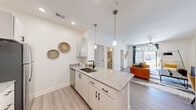 Located at 15000 Penmon Dr in Fuquay-Varina, NC, this thoughtfully designed 2-bedroom, 2-bathroom residence offers a comfortable and modern living experience across a single floor. The open-concept layout seamlessly connects the kitchen, dining area, and living room, creating an inviting and functional space. The kitchen is outfitted with white shaker-style cabinetry, granite countertops, stainless steel appliances including a range with a sleek hood vent, a built-in dishwasher, and a matte black faucet at the undermount sink. Pendant lighting adds a refined touch over the counter peninsula. The living room is bright and airy, featuring light wood-style flooring, a ceiling fan, and sliding glass doors that open to an outdoor area, allowing generous natural light. Both bedrooms feature plush carpeting and a bold two-tone blue wainscoting accent wall, adding a distinctive design element. The spacious primary bedroom includes a well-organized walk-in closet with built-in wire shelving. The bathrooms feature granite-topped vanities and wood-style flooring. A dedicated in-unit laundry area with a full-size washer and dryer adds everyday convenience. The unit includes two closets for ample storage throughout.