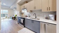 This contemporary 41 square meter apartment in Kelowna, BC, offers a thoughtfully designed living space on a single floor. The kitchen is a standout feature, boasting a sleek two-tone design with light upper cabinets and contrasting grey lower units. It's equipped with stainless steel appliances, including a range and dishwasher, and features a subway tile backsplash and quartz countertops.

The bedroom is bright and airy, with a large window offering mountain views. It's furnished with a queen-sized bed and includes ample closet space. The bathroom is modern and functional, featuring a single vanity with storage, a toilet, and a shower/tub combination.

A notable convenience is the in-unit laundry, with a stacked washer and dryer tucked away in a dedicated space. The apartment's open-concept layout maximizes the use of space, creating a flow between the living areas. Light wood-look flooring throughout adds warmth and continuity to the space.

The apartment's neutral color palette, combined with its contemporary fixtures and fittings, creates a clean, modern aesthetic. This efficient use of space makes it an ideal home for singles or couples looking for a stylish urban living experience in Kelowna.