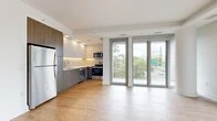 This well-appointed 2-bedroom, 2-bathroom residence offers a thoughtfully designed single-floor layout with a clean, contemporary aesthetic. The open-concept kitchen and living area serves as the heart of the home, featuring light hardwood flooring that flows seamlessly throughout. The kitchen is outfitted with stainless steel appliances, including a range, microwave, and refrigerator, complemented by two-toned cabinetry — warm wood-grain lowers paired with crisp upper cabinets — and a herringbone tile backsplash. A wall of large floor-to-ceiling windows and sliding glass doors floods the living area with natural light and opens to a private balcony with urban and green tree views. The bedrooms are comfortably sized, with the primary bedroom featuring its own dedicated bathroom access. One bedroom offers a full-height window with lush tree views, while the other provides direct hallway access to the second bathroom. Both bathrooms are finished in a modern style, with one featuring large-format stone tile flooring, a wood-toned vanity with LED-lit mirrored medicine cabinet, and a glass-enclosed walk-in shower. A dedicated closet with adjustable shelving provides organized storage. The overall ambiance is bright, clean, and contemporary.