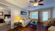 Located at 2042 Arrowgrass Dr in Wesley Chapel, Florida, this single-story home offers a well-designed, open layout with a seamless flow between living spaces. The living room is a warm and inviting area featuring rich hardwood flooring, crown molding, a ceiling fan with light fixture, and large windows dressed with decorative curtains that allow abundant natural light to fill the room. An adjacent dining area continues the hardwood flooring and is defined by an elegant arched entryway, crown molding, a pendant light fixture, and a window with green curtains—a bright and functional space for everyday dining. The kitchen is well-appointed with white cabinetry, granite-style countertops, stainless steel appliances, tile flooring, and a convenient built-in desk nook, providing both practicality and style. The bedroom features plush carpeting, a ceiling fan, and a window with ample natural light. The bathroom includes a single vanity with white cabinetry, tile flooring, and a shower. A dedicated laundry area with a full-size washer and dryer adds everyday convenience. Throughout the home, neutral gray wall tones, crown molding, and consistent finishes create a cohesive and comfortable living environment.