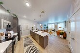 This thoughtfully designed 2-bedroom, 2-bathroom residence is laid out on a single floor, making efficient use of its space. The open-concept kitchen and living area serves as the heart of the home, featuring a sleek kitchen with dark wood cabinetry, a herringbone tile backsplash, stainless steel appliances, and a large center island with a white quartz countertop and bar seating — ideal for casual dining or entertaining. Pendant lighting adds a polished touch overhead. Light wood-style flooring runs throughout the main living area, enhancing the bright, airy feel created by multiple windows and access to a private balcony through glass doors. The living room is generously proportioned, offering ample space for relaxing and gathering. The primary bedroom features a calming color palette with a dedicated walk-in closet and a private en-suite bathroom complete with a walk-in shower. The second bedroom is well-sized with natural light from a large window and its own closet. Both bathrooms are finished with clean, neutral tones and modern fixtures. Throughout the residence, the design balances contemporary style with a warm, livable ambiance.