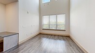 This two-story residence in Lewisville, Texas offers a well-designed layout spread across two floors. The main level features an open-concept living area with wood-style flooring, soaring double-height ceilings, and large windows that invite abundant natural light and views of the surrounding greenery. The modern kitchen is a standout, equipped with stainless steel appliances including a range, microwave, refrigerator, and dishwasher. Sleek gray cabinetry pairs with dark countertops, and a peninsula with a sink provides additional workspace and casual seating. Recessed lighting and a pendant fixture add a polished touch overhead. The spacious living room flows seamlessly from the kitchen, enhanced by tall ceilings and a large window framing outdoor views. Both bedrooms are finished with soft carpet, ceiling fans, and dedicated closets. The primary bedroom is generously sized, while the second bedroom features arched windows that further brighten the space. The full bathroom offers a tiled tub-shower combination, a dark-finished vanity with a rectangular sink, and large-format tile flooring. Two closets and a two-floor layout provide ample storage and functional living throughout this thoughtfully designed home.