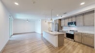 Located at 8000 Windrose Ave in Plano, Texas, this well-appointed single-floor residence offers one bedroom and two bathrooms across a thoughtfully designed layout. The open-concept kitchen and living area serves as the heart of the home, featuring light hardwood-style flooring, recessed lighting, and pendant lights above a central granite island with an undermount sink. The kitchen is equipped with stainless steel appliances, including a French door refrigerator, gas range, and built-in microwave, complemented by taupe cabinetry and a classic white subway tile backsplash. The spacious primary bedroom is carpeted and benefits from natural light through dual windows fitted with blinds, and a ceiling fan overhead. It connects conveniently to a full bathroom featuring warm wood cabinetry, granite countertops, a tiled tub-shower combination, and light hardwood-style flooring. A second bathroom provides a granite vanity and mirror. Additional highlights include a walk-in closet with built-in shelving rods, a hallway with a built-in open shelving unit ideal for storage, and clean white walls throughout that lend a bright, modern ambiance to the entire residence.