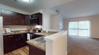 This well-appointed 2-bedroom, 2-bathroom residence is designed for comfortable living across a single floor. The open-concept layout connects the kitchen, dining, and living areas seamlessly, creating a welcoming and functional space. The kitchen is a standout feature, boasting rich dark-wood cabinetry, granite-style countertops, stainless steel appliances including an electric range and built-in microwave, and a peninsula with a built-in sink that doubles as a breakfast bar. Wood-style flooring anchors the kitchen, while plush carpet extends throughout the living areas and bedrooms. The living room is highlighted by a classic fireplace and direct access to a private balcony, where natural light filters in through large sliding glass doors. Both bedrooms are generously sized, featuring soft carpeting, ample closet space, and windows fitted with blinds. The bathrooms are finished with dark wood vanities, granite-style countertops, and tile flooring, complementing the home's consistent design aesthetic. A separate dining area with track lighting adds to the versatility of the layout, making this residence both practical and inviting.