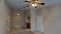 This single-floor space offers a practical and comfortable layout with an open-concept design that connects the living area to the kitchen. The living area features a combination of tile and carpet flooring, providing both durability and comfort underfoot. A ceiling fan with an integrated light fixture is centrally mounted, ensuring efficient air circulation throughout the space. Soft neutral tones on the walls create a clean, welcoming ambiance.

The kitchen is visible from the living area and is defined by warm wood-toned cabinetry and a peninsula-style breakfast bar with a countertop that serves as both a food preparation surface and a casual dining or gathering spot. A pendant light hangs above, adding a focused decorative touch to the kitchen zone. The textured ceiling adds a traditional architectural detail throughout the interior.

A white interior door is positioned within the living area, providing access to an additional room or exterior area. The layout flows openly between spaces, making the interior feel connected and functional. The overall ambiance is understated and practical, with finishes and fixtures that prioritize everyday usability while maintaining a cohesive, neutral aesthetic throughout.