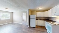 Located at 500 Fair St in Henderson, Kentucky, this single-floor unit offers a practical and comfortable layout with consistent finishes throughout. The kitchen is well-appointed with white shaker-style cabinetry, dark granite-look countertops, a double-basin sink, a white electric range, and a full-size refrigerator — providing ample storage and prep space. The open connection between the kitchen and living area creates a functional flow, with wood-look plank flooring running seamlessly across the main spaces. The living area is generously sized and includes an entry closet alongside the front door, adding convenient storage. The bedrooms are bright and spacious, featuring the same warm wood-look flooring, neutral taupe walls, and windows fitted with horizontal blinds that allow natural light to filter in while maintaining privacy. Views of lush greenery can be seen from the bedroom windows. The bathroom is clean and efficiently designed, featuring a tub-shower combination with a classic surround, a white vanity with a single basin, and a mirrored medicine cabinet. Textured ceilings are present throughout the unit, and neutral wall tones provide a versatile backdrop. The overall ambiance is clean, move-in ready, and well-maintained.
