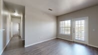 This single-floor residence in San Antonio, TX offers a practical and well-organized layout with four bedrooms, two bathrooms, a kitchen, and a living room. The living area features durable wood-look flooring, neutral-toned walls, and a textured ceiling, with large windows and a glass-panel exterior door that invite abundant natural light and outdoor views. The galley-style kitchen is equipped with warm wood cabinetry, black appliances including a range and refrigerator, light countertops, and a sink with a dishwasher — all set on easy-care hard flooring. The bedrooms offer plush carpeting and neutral walls, with windows providing natural light and exterior views; the primary bedroom includes a dedicated entry door and recessed lighting. Both bathrooms are finished with warm wood vanities, speckled countertops, single-basin sinks, large mirrors, and hard flooring. One bathroom includes a full tub-shower combination with overhead cabinetry for additional storage. Throughout the residence, clean white trim, consistent neutral tones, and practical finishes create a cohesive and move-in-ready aesthetic suited to everyday living.