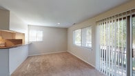 This single-floor residence offers a well-organized layout designed for comfortable everyday living. The spacious living area is finished with neutral-toned carpet and features a large sliding glass door flanked by a wide window, allowing generous natural light and views of the surrounding greenery. A secondary window further brightens the space, creating an open and airy atmosphere throughout.

The kitchen is equipped with white cabinetry, a full suite of appliances including a refrigerator, electric range, and dishwasher, complemented by a classic tile backsplash and warm hardwood flooring. A window above the sink adds additional light to the functional workspace.

The bedrooms are carpeted and finished in soft, neutral tones. One bedroom features multiple windows on adjacent walls and a walk-in closet, providing ample storage. Additional bedrooms offer individual windows with views of the exterior and are well-suited for a variety of uses.

The bathroom is cleanly finished with white tile surrounding a full tub-and-shower combination, chrome fixtures, and hardwood flooring, lending a crisp, functional aesthetic. Clean white trim and consistent neutral wall tones unify the interior throughout, creating a cohesive and move-in ready living environment.