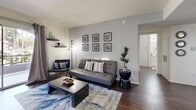 Located at 3900 E Sunset Rd in Las Vegas, NV, this well-designed one-bedroom unit makes smart use of its compact footprint across a single floor. The open-concept living and dining area serves as the heart of the home, featuring rich hardwood-style flooring, neutral gray walls, and a sliding glass door that opens to a private balcony, allowing natural light to fill the space and offering pleasant outdoor views. The living area flows seamlessly into a dedicated dining space and a galley-style kitchen outfitted with white cabinetry, granite-style countertops, and a full suite of white appliances including a gas range, microwave, and refrigerator — all contributing to a clean, functional aesthetic. The bedroom is a comfortable retreat with plush carpeting, a ceiling fan, a natural light-admitting window with draping curtains, and direct access to a walk-in closet, providing ample storage. The unit also includes a dedicated laundry area for added convenience. Throughout the space, consistent design choices — including coordinated gray tones, hardwood-style flooring in common areas, and carpeted bedroom — create a cohesive and inviting atmosphere well-suited for everyday living in Las Vegas.