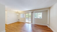 This single-floor, 2-bedroom, 1-bathroom unit is designed with a practical and cohesive layout. Warm-toned hardwood flooring runs consistently throughout the entire space, lending a unified and inviting aesthetic. The combined living and dining area serves as the central gathering space, bathed in natural light through multiple windows fitted with horizontal blinds and a sliding glass door that opens to a private balcony with outdoor views of surrounding greenery.

The kitchen is efficiently arranged, featuring stainless steel appliances including a range, over-the-range microwave, and light-toned countertops with white cabinetry. A bi-fold pantry door provides additional storage within the compact kitchen footprint.

The primary bedroom offers a comfortable amount of space, complemented by a double sliding-door closet and natural light from windows overlooking the outdoors. The second bedroom, slightly smaller, includes its own window and a ceiling-mounted light fixture. Both rooms feature the same hardwood flooring found throughout the unit.

The bathroom is finished in a clean, all-white palette featuring a pedestal sink, a framed mirror with overhead lighting, white tile wainscoting, and a glass-door shower enclosure, creating a bright and functional space.