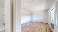 Located at 43321 Sierra Highway in Lancaster, CA, this single-floor studio unit offers an efficiently designed layout that includes a living area, a kitchenette, and a full bathroom. The main living space is bright and open, anchored by warm-toned hardwood-style flooring that runs throughout the unit. A large sliding window allows generous natural light to fill the room while offering views of the surrounding greenery outside. A wall-mounted air conditioning unit provides climate control, complemented by a baseboard heater along the opposite wall. The textured popcorn ceiling and clean white walls create a neutral, move-in-ready aesthetic. A sliding-door closet provides built-in storage within the living area. The kitchenette is neatly tucked into a dedicated nook and features white cabinetry, a stainless steel sink, and a range, making efficient use of the available space. The bathroom is well-appointed with a gray vanity cabinet, a white countertop sink, a large mirror, and a tiled tub-shower combination with clean white tile surround. Consistent hardwood-style flooring carries through into the bathroom, tying the unit together with a cohesive look. This unit is ideally suited for a single occupant seeking a clean, functional living space in Lancaster.