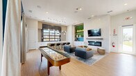 Located in Celina, TX, this single-floor community space is a thoughtfully designed gathering hub that blends contemporary style with welcoming functionality. The open-plan living and kitchen area serves as the heart of the space, where light hardwood flooring and bright white walls create a clean, modern backdrop throughout.

The kitchen area is anchored by a long white quartz island with bar seating, complemented by crisp white shaker cabinetry, stainless steel appliances, and a beverage refrigerator. A striking black-framed glass panel window floods the kitchen with natural light and provides views of the surrounding neighborhood. A cluster of glass pendant lights adds a refined industrial touch overhead. A neon "Drinks on Us" sign adorns a lush green living wall, adding a playful, inviting accent to the space.

The living area features a sleek linear electric fireplace set into a textured white tile feature wall, with a wall-mounted television above. Comfortable seating arrangements, a natural wood coffee table, and a full-size shuffleboard table make the space ideal for socializing and recreation. A bold teal accent wall, a cork pinboard, and framed artwork contribute character and warmth.

The accessible restroom is finished with classic white subway tile wainscoting, neutral floor tile, and grab bars, ensuring comfort and compliance for all users.