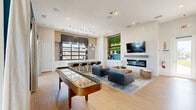 Located in Celina, TX, this single-floor community space is a thoughtfully designed gathering hub that blends contemporary style with welcoming functionality. The open-plan living and kitchen area serves as the heart of the space, where light hardwood flooring and bright white walls create a clean, modern backdrop throughout.

The kitchen area is anchored by a long white quartz island with bar seating, complemented by crisp white shaker cabinetry, stainless steel appliances, and a beverage refrigerator. A striking black-framed glass panel window floods the kitchen with natural light and provides views of the surrounding neighborhood. A cluster of glass pendant lights adds a refined industrial touch overhead. A neon "Drinks on Us" sign adorns a lush green living wall, adding a playful, inviting accent to the space.

The living area features a sleek linear electric fireplace set into a textured white tile feature wall, with a wall-mounted television above. Comfortable seating arrangements, a natural wood coffee table, and a full-size shuffleboard table make the space ideal for socializing and recreation. A bold teal accent wall, a cork pinboard, and framed artwork contribute character and warmth.

The accessible restroom is finished with classic white subway tile wainscoting, neutral floor tile, and grab bars, ensuring comfort and compliance for all users.