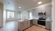 Located at 3204 SW 12th Ave in Portland, Oregon, this single-floor unit presents a clean, contemporary design throughout. The open-concept layout connects the kitchen and living area seamlessly, creating a spacious and functional environment. The kitchen is a standout feature, equipped with stainless steel appliances including an electric range, microwave, dishwasher, and refrigerator. Gray cabinetry with modern hardware pairs with white countertops, while a peninsula with an integrated sink adds additional workspace and casual dining potential. Recessed lighting and a wall-mounted mini-split system provide comfort and efficiency throughout the main living area, which also features a ceiling fan.

The living space flows into carpeted bedroom areas, one of which includes a sliding-door closet and a spacious walk-in closet outfitted with wire shelving. Two bathrooms serve the unit: one features a tub-shower combination with tiled surround and a white vanity, while the other offers a glass-enclosed walk-in shower and a light blue vanity with ample drawer storage. Both bathrooms include hardwood-style flooring and large mirrors. Natural light filters in through multiple windows, contributing to the unit's bright and welcoming ambiance throughout.