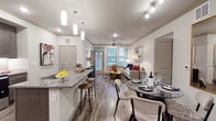 This thoughtfully designed single-floor residence offers a seamless open-concept layout connecting the kitchen, dining, and living areas into one cohesive, light-filled space. The gourmet kitchen is a standout feature, showcasing rich dark cabinetry, granite countertops, a subway tile backsplash, stainless steel appliances, and a large island with bar seating — ideal for both cooking and casual entertaining. Pendant lighting above the island adds a refined touch, while wood-style flooring runs throughout the main living areas, enhancing the modern aesthetic. The dining area accommodates a full table setting, and the living room offers ample space with crown molding, a ceiling fan, and large windows that invite natural light and outdoor views. Two well-sized bedrooms provide comfortable retreats; one features an en suite bathroom with a double granite vanity and a spacious walk-in closet, while the second bathroom includes a soaking tub with tiled surround. Both bathrooms are finished with dark cabinetry and granite counters, consistent with the home's design language. A dedicated in-unit laundry closet with full-size washer and dryer adds everyday convenience. Overall, the space presents a polished, contemporary ambiance with upscale finishes at every turn.