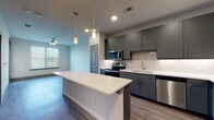 Located at 1502 Blue Ridge Dr in Georgetown, Texas, this single-story home showcases a clean, modern design with thoughtfully selected finishes throughout. The open-concept layout connects the living area to a well-appointed kitchen, creating a functional and inviting atmosphere. The kitchen is a standout feature, equipped with sleek gray cabinetry, a herringbone-patterned tile backsplash, white quartz countertops, and a full suite of stainless steel appliances including a refrigerator, range, microwave, and dishwasher. A central island with pendant lighting above provides additional workspace and a casual dining option. Warm-toned wood-look flooring flows throughout the main living spaces, complementing the neutral wall tones and recessed lighting. Natural light enters generously through windows fitted with horizontal blinds. The bedroom offers a comfortable, well-proportioned space with the same wood-look flooring and a large window. The bathroom is finished with light marble-style tile on both the floors and tub surround, paired with a gray vanity topped with a white surface and a curved shower rod. The overall ambiance is fresh, contemporary, and move-in ready, reflecting a cohesive modern aesthetic suited for comfortable everyday living.