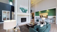 The clubhouse at Resort At Lake Crossing is a thoughtfully designed communal space that combines sophisticated style with an open, welcoming atmosphere. The centerpiece of the main lounge is a dramatic floor-to-ceiling white brick fireplace, topped with bold abstract artwork that echoes the space's signature green and neutral color palette. Soaring vaulted ceilings amplify the sense of grandeur, while light wood-tone flooring runs throughout, lending warmth and continuity across zones.

The lounge area is furnished with plush dark teal sofas, gray accent chairs, and a substantial wood coffee table, creating an inviting setting for relaxation or socializing. Large multi-pane windows and glass-paneled double doors flood the interior with natural light and offer views of the surrounding landscape. An arched transom window above the entry doors adds an architectural flourish.

Adjacent to the lounge, a bar-height counter with metal stools connects seamlessly to a full kitchen finished with white cabinetry and stainless steel appliances, highlighted by a vibrant green accent wall. A separate dining nook with bistro-style seating sits beside bright windows. Bold color-blocking — combining navy, green, and white — gives the entire space a distinctive, modern resort aesthetic.