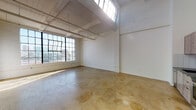 Located at 443 San Pedro St in the heart of Downtown Los Angeles, this single-floor industrial loft blends raw architectural character with contemporary updates. Soaring ceilings with exposed white-painted wood beams and structural pipe runs define the open main living area, which is bathed in natural light through large, multi-pane industrial steel-framed windows overlooking the city. Polished concrete floors extend throughout, adding to the loft's urban aesthetic.

The kitchen is outfitted with light wood cabinetry, dark countertops, a white subway tile backsplash, and a full suite of stainless steel appliances including a refrigerator, range, microwave, and dishwasher. A dedicated enclosed room provides flexible space for a bedroom or private office, featuring its own high ceilings and access to natural light through a skylight above.

The bathroom is finished to a high standard, featuring a wood-toned vanity with dark countertop, matte black fixtures, a framed mirror, and a generously sized glass-enclosed walk-in shower clad in white mosaic tile. An additional half bath with matching finishes offers added convenience. The overall ambiance is open, airy, and industrial-modern, ideal for creative or live-work use in a vibrant urban setting.