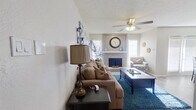 This single-story, 1-bedroom, 1-bathroom home offers a thoughtfully designed layout that maximizes every square foot of its compact footprint. The living room serves as the heart of the home, showcasing a tile-surround fireplace framed by a shiplap accent wall, ceiling fan with light fixture, and textured ceilings. Natural light filters in through multiple windows dressed with white plantation shutters, creating a bright and welcoming atmosphere. Hardwood-style flooring runs through the main living areas, adding warmth and continuity. Adjacent to the living room, the dining area features a mirrored wall that amplifies the sense of space, along with French doors that bring in additional natural light. The bedroom is carpeted for comfort and includes a ceiling fan, a generous walk-in closet with built-in shelving, and a window for natural light. The bathroom is well-equipped with warm wood cabinetry, a granite-style countertop, a large vanity mirror, and a shower-tub combination. The entrance provides a functional transition into the home. Overall, the space presents a cohesive, neutral color palette with tasteful details that balance comfort and practicality throughout.