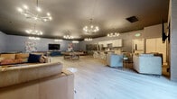 Located at 8820 S Hosmer St in Tacoma, WA, this single-floor community clubhouse offers a generously sized, open-concept layout designed for gathering, recreation, and relaxation. Light hardwood flooring runs throughout the space, complemented by dark painted ceilings and gray painted concrete block walls that give the interior a modern, industrial character. Multiple statement chandeliers provide warm, ambient lighting across the entire floor.

The fully equipped kitchen features white shaker cabinetry, marble-look countertops, a large center island with bar seating, stainless steel appliances including a full-size refrigerator, and a microwave — ideal for hosting events. Adjacent to the kitchen, a dedicated dining area includes a solid wood table with seating and a striking triptych of framed abstract artwork on the wall.

The living and lounge areas are thoughtfully arranged to serve multiple functions simultaneously. One lounge features leather sofas, arched mirrors, and a bold area rug, while another hosts a large sectional sofa with a wall-mounted television and vibrant art. The game area includes a billiards table and foosball table, adding an entertaining focal point to the space. A large picture window brings in natural light and views of the surrounding grounds. The space also includes a fully accessible bathroom with grab bars, a vanity, and hardwood-style flooring.
