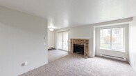 Located in Silverdale, Washington, this single-floor unit offers a well-organized layout designed for comfortable everyday living. The living room serves as the heart of the home, anchored by a classic brick fireplace and finished with plush carpet underfoot. Sliding glass doors open to an outdoor balcony area, while a large picture window fills the room with natural light and garden views, creating a bright and inviting atmosphere. Baseboard heating is featured throughout the carpeted areas.

The galley-style kitchen is thoughtfully appointed with warm wood cabinetry, granite-toned countertops, a full suite of black appliances including a range, refrigerator, and dishwasher, and durable wood-look flooring that extends through the space.

The bedrooms are generously sized with soft carpet, natural window light, and ample closet storage, including both reach-in and walk-in configurations with built-in shelving and hanging rods. The bathroom is well-appointed with rich wood cabinetry, granite-style countertops, a single vanity sink, and wood-look vinyl flooring, complemented by a shower-tub combination. The overall design is clean, neutral, and move-in ready.