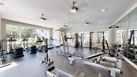 Located in Charlotte, NC, this fitness center offers a generously sized, single-floor exercise room designed to accommodate a comprehensive range of workout routines. The space features durable rubber flooring throughout, providing a safe and functional surface for all types of training activities.

Natural light pours in through multiple large, white-framed windows that line the walls, creating a bright and welcoming atmosphere. Several ceiling fans are mounted overhead, complementing the recessed lighting to ensure comfortable airflow and visibility throughout the room.

The facility is outfitted with an impressive array of equipment. Cardio options include treadmills, elliptical machines, stationary bikes, and WaterRower rowing machines. For strength training, the space provides a multi-station cable machine, a power tower, a weight bench, a barbell setup, and a full rack of dumbbells ranging across multiple weight increments. A wall-mounted flat-screen television adds entertainment for those engaged in longer workout sessions.

Floor-to-ceiling mirrors span one wall, visually expanding the space while allowing users to monitor their form. The overall design balances a clean, neutral color palette of whites and light grays with a practical, gym-ready layout, resulting in a well-appointed fitness environment that is both functional and inviting.