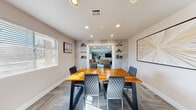 Located at 2301 S Valley View Blvd in Las Vegas, NV, this single-floor space offers a well-designed layout comprising a living room and a dining room, each thoughtfully finished with modern, cohesive aesthetics.

The dining room features a striking solid wood dining table paired with quilted charcoal chairs, set atop patterned carpet flooring. Recessed ceiling lights provide bright, even illumination, while textured accent walls flanking a central passageway add visual depth. Built-in wall shelving displays curated greenery and decorative objects, and a window with horizontal blinds allows natural light to filter in.

The living room is open and inviting, anchored by a warm cognac leather sofa and accented with an orange accent chair. Natural light pours through multiple windows with white blinds, casting patterned light across the carpet. A metal and wood open shelving unit, gold decorative wall accents, and a wall-mounted TV contribute to the room's modern character. A wall-mounted mini-split unit ensures climate comfort, and a glass-paned barn-style sliding door adds an industrial touch connecting the spaces.

Together, the rooms create a functional and visually unified environment with a contemporary design sensibility, making this Las Vegas space both practical and aesthetically refined.