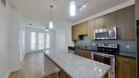 This well-appointed 1-bedroom, 1-bathroom unit offers a thoughtfully designed layout across a single floor. The open-concept kitchen serves as a central highlight, featuring warm wood cabinetry, a decorative mosaic tile backsplash, stainless steel appliances including a range, microwave, and dishwasher, and a generous granite-topped island with pendant lighting overhead. The kitchen flows seamlessly into the living area, which is finished with light hardwood-style flooring, a ceiling fan, and large windows fitted with blinds that invite abundant natural light.

The bedroom offers a comfortable and serene retreat, carpeted for warmth and comfort, with a ceiling fan and a window providing additional natural light. A dedicated closet provides practical storage. The full bathroom is well-equipped with a wood-toned vanity, dark granite countertop, a large mirror with overhead lighting, a combined shower and soaking tub with tile surround, built-in open shelving, and hardwood-style flooring. Throughout the unit, a clean, neutral color palette of crisp whites and warm wood tones creates a modern and cohesive aesthetic, making the space feel bright, functional, and move-in ready.