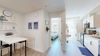 Located in San Diego's vibrant 92102 neighborhood, this two-story, 2-bedroom, 2-bathroom home offers a thoughtfully designed layout spread across two levels. The ground floor serves as a welcoming entry point, while the upper floor houses the majority of the living space. Light wood-tone flooring flows throughout, complementing the crisp white walls and creating a clean, modern aesthetic.

The open-plan kitchen and living area is a central highlight of the upper floor. The galley-style kitchen is well-appointed with white cabinetry, quartz countertops, black appliances including a side-by-side refrigerator, electric range, microwave, and dishwasher, as well as a sleek black fixtures sink. The adjacent living area is bright and airy, bathed in natural light from large windows, and provides a comfortable, inviting atmosphere.

A hallway connects the bedrooms, both of which are naturally lit and feature clean white walls. The primary bedroom offers a cozy, well-proportioned retreat. Both bathrooms are finished with light wood-tone flooring and white vanities; one bathroom features an accessibility-friendly roll-in shower with grab bars and a fold-down seat. A stacked in-unit washer and dryer adds everyday convenience. Staircases connect the two floors, completing this efficiently designed San Diego home.