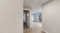 This single-story home offers a thoughtfully designed layout across three bedrooms and two full bathrooms. The interior is finished with a clean, neutral color palette of soft grays and whites, creating a bright and cohesive aesthetic throughout. Light hardwood-style flooring runs through the main living areas, complemented by plush carpeting in the bedrooms for added comfort.

The open living area is bathed in natural light from large windows and features a private exterior door, adding to the airy, welcoming atmosphere. The kitchen is a standout space, outfitted with crisp white shaker-style cabinetry extending to the ceiling for ample storage, a white quartz countertop with a breakfast bar overhang, a white subway tile backsplash, and a full suite of stainless steel appliances including a refrigerator, range, and built-in microwave.

The bedrooms are comfortably sized, with the primary bedroom offering generous closet space. One bedroom features a mirrored sliding-door closet and a ceiling fan, while another provides a quieter, more compact retreat. The bathrooms are finished with white cabinetry, brushed nickel fixtures, and clean tilework. A central hallway connects the bedrooms and bathrooms, ensuring a practical and functional flow throughout the home.