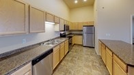 This single-floor residence is designed with an open-concept layout that seamlessly connects the kitchen and living area, creating a spacious and functional environment. The living space features vaulted ceilings that amplify the sense of openness, with plush carpeting underfoot and baseboard heating along the walls. Natural light filters in through multiple windows, including a glass-paneled exterior door, enhancing the bright, neutral interior palette.

The kitchen is well-appointed with light wood cabinetry extending to the upper walls, dark granite-style countertops, and a full suite of stainless steel appliances including a refrigerator, electric range, microwave, and dishwasher. A kitchen island provides additional prep and storage space, while tile flooring distinguishes this area from the carpeted living zone.

Two bathrooms serve the unit. The first includes a full soaking tub with shower combination, a single-sink vanity with granite-style countertops, and tile flooring. The second bathroom features a walk-in shower stall, a matching vanity, and consistent tile flooring. Both are finished in neutral tones.

The bedroom is a comfortable, carpeted room with a window offering natural light and baseboard heating. A dedicated in-unit laundry closet houses a full-size washer and dryer, adding everyday convenience to this well-designed space.