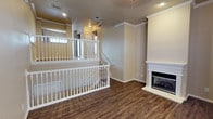 This single-floor space combines classic design elements with functional layout to create a cohesive and inviting interior. The flooring throughout is a rich, dark hardwood-style material that adds warmth and visual depth to the space. Crown molding runs along the upper walls and ceiling, contributing a refined, traditional aesthetic.

A standout feature of the main living area is the white-mantled fireplace, which serves as a natural focal point on one wall. Its clean, classic surround complements the neutral warm-gray wall tones found throughout the space.

A staircase with white-painted balusters and railings is prominently positioned within the layout, with an open railing design that allows sightlines across the space and maintains an airy, open feel. The upper landing area near the staircase is well-defined, with additional railing enclosing the space safely.

Recessed lighting is installed throughout the ceiling, providing consistent, even illumination across the interior. Ceiling vents are also visible, indicating a central HVAC system. The overall ambiance is clean, neutral, and move-in ready, with a timeless design sensibility that balances comfort and practicality.