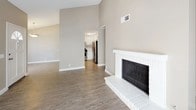 This single-floor residence offers a thoughtfully designed layout with a blend of warm neutrals and modern finishes throughout. The living area makes an immediate impression with its vaulted ceilings, wood-look vinyl flooring, and a classic white brick fireplace that serves as a focal point. Large vertical-blind-covered sliding glass doors flood the space with natural light and provide outdoor access. The kitchen is well-equipped, featuring crisp white cabinetry with matte black hardware, light countertops, wood-look vinyl flooring, and a full suite of stainless steel appliances including a gas range and refrigerator. A dedicated in-unit laundry area accommodates a full-sized washer and dryer side by side, with overhead shelving for added storage. The bedrooms are carpeted in a neutral tone and receive natural light through sliding or standard windows. A carpeted hallway connects the bedroom wing, which includes two bathrooms finished with white vanities, light countertops, matte black hardware, tub-shower combinations, and wood-look vinyl flooring. Textured ceilings and white trim are consistent throughout, lending a cohesive and clean aesthetic to the entire space.
