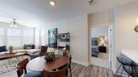 This single-story residence is thoughtfully designed with a contemporary aesthetic and a practical open-concept layout. The main living and dining area is unified by durable wood-look flooring, with large windows fitted with blinds that allow ample natural light to fill the space. A ceiling fan overhead and a dedicated dining area with a round wooden table complement the living room, which offers comfortable seating and wall art that adds visual interest.

The kitchen is a standout feature, showcasing dark, flat-front cabinetry that extends to ceiling height, a subway tile backsplash, and a full suite of stainless steel appliances, including a refrigerator, range, and microwave. A spacious island with a white countertop and bar seating serves as both a functional workspace and a casual gathering spot, with pendant lighting above.

Two bedrooms are carpeted and each includes a ceiling fan, natural light from windows, and ample room for furnishings. The bathroom features dark cabinetry with a white countertop, wood-look flooring, and clean, neutral finishes. Throughout the unit, a cohesive neutral color palette and modern detailing create a polished, inviting atmosphere.