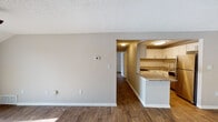 This single-story residence is designed with a practical, open layout that connects the living areas through a series of well-proportioned rooms unified by dark hardwood-style flooring and neutral gray-toned walls. Textured ceilings run throughout, complementing the clean white baseboards that frame each space.

The living area is generously sized, offering ample room for a variety of furniture arrangements. A sliding glass door at one end allows natural light to filter in, while a ceiling fan provides overhead circulation. The space flows directly toward a hallway that connects the bedrooms and additional rooms.

The kitchen is a notable feature, showcasing white shaker-style cabinetry, granite countertops, and a white subway tile backsplash. A gas range anchors the cooking area, while a peninsula counter with matching granite serves as a functional transition between the kitchen and the adjacent living space.

The bedrooms are well-sized, each equipped with ceiling fans and closets. One bedroom includes a dedicated walk-in closet with wire shelving and in-unit laundry hookups conveniently integrated within.

The bathroom features a granite-topped vanity, a standard tub and shower combination, and consistent hardwood-style flooring that carries throughout the unit.