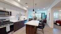Located in Chula Vista, CA, this single-story residence showcases a thoughtfully designed open-concept floor plan with contemporary finishes throughout. The kitchen is a standout feature, equipped with stainless steel appliances including a French door refrigerator, gas range, and built-in microwave. Two-tone cabinetry pairs rich walnut-finish lower cabinets with crisp white upper cabinets, complemented by a white quartz countertop and subway tile backsplash. A central island with bar seating and pendant lighting above creates an ideal space for dining and entertaining. Light wood-style flooring flows through the main living areas, connecting the kitchen seamlessly to the dining and living spaces. The living room is bright and welcoming, benefiting from generous natural light through large windows and direct access to an outdoor area via a glass-panel door. The bedrooms feature plush carpeting and well-sized windows with blinds for privacy. Two bathrooms mirror the home's modern aesthetic, each featuring walnut-finish vanities, white quartz countertops, large framed mirrors, and tile surrounds. Built-in shelving in one bathroom adds practical storage. The overall design balances clean, modern lines with warm wood tones, creating a cohesive and inviting atmosphere throughout.