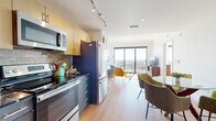 This well-appointed single-floor unit showcases a thoughtfully designed open-concept layout that seamlessly connects the kitchen, dining, and living areas. Light hardwood flooring runs throughout, contributing to a warm and cohesive aesthetic.

The kitchen is outfitted with stainless steel appliances — including a refrigerator, electric range, and built-in microwave — complemented by two-tone cabinetry featuring light upper cabinets and dark lower units, a textured stone tile backsplash, and dark countertops. Track lighting overhead adds both function and style.

The dining area features a round glass-top table paired with mid-century modern upholstered chairs in earthy olive and sage tones. The open living room is bathed in natural light from floor-to-ceiling sliding glass doors that frame expansive panoramic views of the surrounding cityscape and treetops, creating a striking focal point.

The bedroom continues the bright, airy feel with its own large window offering outdoor views, light hardwood floors, and ample space. The full bathroom is finished with marble-look tile flooring, a wood vanity with dark countertop, a backlit mirror, and a tub-shower combination. Throughout, the space maintains a clean, contemporary aesthetic accented by mid-century modern design elements.