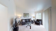 This single-floor residence offers a thoughtfully designed layout that balances comfort and functionality across its key living spaces. The living room immediately draws attention with its striking vaulted ceilings, creating an open and airy atmosphere. Plush carpeting, neutral walls, and a large window allowing natural light enhance the welcoming ambiance, while the space comfortably accommodates a full seating arrangement centered around a glass coffee table.

Adjacent to the living area, a dedicated dining space features a glass-top dining table set beneath an elegant chandelier, with a window providing additional natural light and a view of surrounding greenery.

The kitchen is outfitted with rich, dark wood cabinetry, granite countertops, and stainless steel appliances including a range, over-the-range microwave, and refrigerator — offering both style and practicality for everyday cooking.

The bedroom is a serene retreat, appointed with soft carpeting, dual bedside tables with matching lamps, and windows that invite natural light. The room provides access to two separate doorways, suggesting a private en-suite bathroom and a closet or additional room for added convenience.

The bathroom features a granite-topped vanity with a wide mirror and Hollywood-style lighting, complemented by a shower area visible in the reflection. Throughout the space, a consistent neutral palette and modern finishes create a cohesive, polished aesthetic.