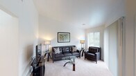 This single-floor residence offers a thoughtfully designed layout that balances comfort and functionality across its key living spaces. The living room immediately draws attention with its striking vaulted ceilings, creating an open and airy atmosphere. Plush carpeting, neutral walls, and a large window allowing natural light enhance the welcoming ambiance, while the space comfortably accommodates a full seating arrangement centered around a glass coffee table.

Adjacent to the living area, a dedicated dining space features a glass-top dining table set beneath an elegant chandelier, with a window providing additional natural light and a view of surrounding greenery.

The kitchen is outfitted with rich, dark wood cabinetry, granite countertops, and stainless steel appliances including a range, over-the-range microwave, and refrigerator — offering both style and practicality for everyday cooking.

The bedroom is a serene retreat, appointed with soft carpeting, dual bedside tables with matching lamps, and windows that invite natural light. The room provides access to two separate doorways, suggesting a private en-suite bathroom and a closet or additional room for added convenience.

The bathroom features a granite-topped vanity with a wide mirror and Hollywood-style lighting, complemented by a shower area visible in the reflection. Throughout the space, a consistent neutral palette and modern finishes create a cohesive, polished aesthetic.