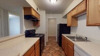This single-floor residence offers a well-organized layout with distinct living, cooking, sleeping, and bathing areas. The galley-style kitchen is lined on both sides with warm honey-toned wood cabinetry, light countertops, and a suite of black appliances including a coil-top electric range and a full-size refrigerator. A stainless steel sink sits opposite the range, and the distinctive terracotta-toned geometric tile flooring adds character to the space. The kitchen connects directly to a hallway leading further into the unit.

The open living area features the same terracotta tile flooring that transitions into plush wall-to-wall carpeting. A wood-burning fireplace serves as a focal point along one wall, while a ceiling fan and access to a windowed exterior door allow for natural light and ventilation. The space flows naturally toward the private areas of the home.

The bedrooms are carpeted and finished with neutral tones, textured ceilings, and ceiling fans, creating a calm and restful atmosphere. One bedroom receives natural light through a window overlooking greenery outside.

The bathroom includes a full tub-and-shower combination with tiled surround, a standard vanity with mirror, and consistent terracotta-style tile flooring that ties the home together visually. The overall aesthetic is practical and cohesive throughout.