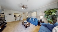 This single-floor residence offers a thoughtfully designed layout that balances comfort and functionality. The living room serves as the heart of the home, featuring plush carpeting, soft blue-gray walls, and crown molding that adds a refined touch. A ceiling fan overhead provides practical comfort, while the open pass-through to the kitchen creates a connected, sociable flow. The kitchen is well-equipped with warm honey-toned cabinetry, granite-style countertops, and a full suite of black appliances including a range, microwave, dishwasher, and refrigerator. Light hardwood-style flooring brightens the space, and a raised breakfast bar with bar seating adds a casual dining option. The entryway transitions seamlessly into the living area, maintaining the home's cohesive, welcoming aesthetic. The bedroom is a serene retreat, complete with carpeted flooring, crown molding, a ceiling fan, and windows that allow natural light to filter in. The bathroom features tile flooring, a generous vanity with granite-style countertops, ample cabinetry, and a shower-tub combination. Throughout the residence, a consistent cool, neutral color palette creates a calm and inviting atmosphere.