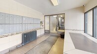 Located at 2417 Hurontario Street in Mississauga, this single-floor lobby entrance serves as the primary access point for the building. The space is efficiently arranged, making practical use of its compact footprint. Large, floor-to-ceiling windows with dark aluminum frames dominate one wall, flooding the interior with natural light and offering views of Hurontario Street and the surrounding neighbourhood. An automated sliding entrance door provides easy access from the exterior.

The interior finishes are clean and functional, featuring large-format light grey floor tiles and white block-style wall tiles accented by a decorative mosaic tile border that runs horizontally along the lower wall section. An array of grey individual mailboxes is mounted along one wall, accommodating the building's residents. A Canada Post parcel locker unit stands nearby, providing secure package delivery access. A cast-iron radiator beneath the mailboxes provides supplemental heating during colder months.

The lobby connects directly to an interior stairwell via glazed doors, facilitating easy movement through the building. A security camera is mounted near the entrance, and an intercom panel is positioned conveniently by the mailboxes. The overall ambiance is practical, bright, and well-maintained.