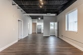 Located at 1230 Second Ave in Columbus, Georgia, this single-floor unit blends industrial design elements with modern finishes throughout. A striking feature across the main living and kitchen areas is the exposed black ceiling structure, which adds an urban, loft-inspired character while allowing for generous ceiling height. Dark hardwood-style flooring runs through the kitchen, hallways, and bathrooms, providing a cohesive and durable foundation.

The kitchen is well-appointed with white shaker cabinetry, granite-style countertops, and a full suite of stainless steel appliances including a refrigerator, electric range, microwave, and dishwasher. A window above the sink offers views of the surrounding downtown Columbus streetscape, filling the space with natural light.

The bedrooms feature neutral carpet, large windows fitted with blinds, and the same dramatic exposed ceiling treatment seen elsewhere. One bedroom connects directly to a private bathroom with a white vanity, hardwood-style flooring, and a glass-enclosed tile shower. A second full bathroom mirrors this refined aesthetic.

A dedicated in-unit laundry closet houses a stacked washer and dryer, adding everyday convenience. Throughout, neutral wall tones and clean white trim create a bright, modern atmosphere suited for a variety of uses.