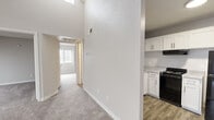 This single-floor, 2-bedroom unit offers a practical and well-organized layout making efficient use of its space. The kitchen is a standout area, featuring crisp white shaker-style cabinetry that extends to the upper walls for ample storage, light-toned stone countertops, and a full suite of black appliances including a gas range, dishwasher, and refrigerator. Wood-look vinyl flooring in the kitchen adds a clean, durable finish that contrasts neatly with the cabinetry. A partial wall visually separates the kitchen from the carpeted hallway and living areas, which are finished in neutral gray tones throughout. The primary bedroom is generously sized, featuring soft wall-to-wall carpeting, a textured ceiling, and a dedicated closet with built-in shelving for organized storage. The second bedroom mirrors this layout with its own closet and a window that invites natural light. Both rooms maintain a calm, neutral palette well-suited for versatile furnishing. A notable architectural detail is the high vaulted ceiling near the entry, visible in the hallway, which adds an unexpected sense of openness to the unit. Overall, the space presents a clean, move-in-ready environment with functional design throughout.