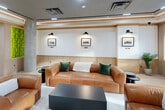 Located at 4414 Douglaston Parkway in Douglaston, NY, this thoughtfully designed lounge offers a refined communal retreat across a single floor. The space is composed of a living room, dining area, and connecting hallway, all unified by a cohesive modern aesthetic rooted in warm, neutral tones.

The living room serves as the centerpiece, featuring light wood-toned flooring, a tray ceiling with recessed and track lighting, and white shiplap-style wall paneling accented by natural wood trim. Rich cognac leather sofas and armchairs are arranged around a dark coffee table, creating an inviting seating arrangement. A built-in entertainment wall houses a large flat-screen TV above a sleek linear fireplace, flanked by illuminated open shelving displaying decorative objects and books. A vibrant living moss wall adds a striking natural accent.

Multiple windows allow ample natural light to filter in, while wall-mounted sconces and framed artwork contribute to a curated, gallery-like atmosphere. A structural column adds an architectural element to the room.

An outdoor terrace accessible from the lounge features lounge chairs behind glass-panel railings, offering views of the surrounding Douglaston neighborhood. The hallway connects the spaces with the same seamless, polished finishes found throughout, ensuring a consistent and welcoming environment from entry to exit.