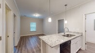 Located at 149 Sierra Vista Cir in Cornelia, Georgia, this single-floor residence offers a well-designed, open layout that maximizes functionality and comfort. The kitchen serves as a central highlight, featuring a large granite-topped island with an integrated sink, crisp white cabinetry, and a full suite of black appliances including a refrigerator, electric range, over-the-range microwave, and dishwasher. Stylish pendant lights hang above the island, providing focused task lighting while adding a modern aesthetic touch. Crown molding accents the main living and kitchen areas, elevating the overall finish of the space. Durable hardwood-style flooring runs consistently throughout the unit, contributing to a cohesive and easy-to-maintain interior. The bedrooms are well-proportioned, with neutral wall tones and ample natural light. One bedroom includes a convenient en-suite bathroom, while a closet with built-in shelving provides organized storage in another bedroom. The bathrooms are finished with granite-topped vanities, white cabinetry, and full tub-shower combinations. The neutral color palette and clean finishes throughout create a bright, move-in-ready environment suited for a variety of lifestyles.