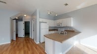 Located at 15300 Dismuke Ave in Biloxi, Mississippi, this two-story home offers a thoughtfully designed layout with a blend of hardwood and tile flooring throughout. The entry foyer welcomes visitors with clean lines, neutral gray walls, and a seamless transition between wood and tile surfaces.

The open-concept kitchen is well-appointed with white cabinetry, a peninsula countertop with a wraparound laminate surface, white appliances including a refrigerator, range, and microwave, and track lighting overhead. The kitchen flows naturally into the dining and living area, which is bathed in natural light from large windows and a sliding glass door that opens onto a rear deck, providing outdoor views of the surrounding greenery. A chandelier adds a decorative touch to the dining space.

A bathroom on the main level features a dual-sink vanity with white cabinetry, tile flooring, a soaking tub, and a separate toilet area. The upper floor, visible in the dollhouse view, includes multiple rooms with hardwood flooring, ample windows for natural light, and a staircase connecting both levels. The attached single-car garage provides convenient interior access and additional storage space. Throughout the home, a consistent soft gray color palette creates a calm, cohesive ambiance.