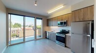 Located at 1280 SE Nehalem St in Portland, Oregon, this thoughtfully designed single-floor residence offers a clean, modern aesthetic throughout. The open kitchen is a standout feature, equipped with a full suite of stainless steel appliances including a gas range, built-in microwave, dishwasher, and refrigerator. Warm wood-tone cabinetry pairs with light countertops and a classic white tile backsplash, creating a functional and visually appealing space. Light vinyl plank flooring runs seamlessly through the main living and kitchen areas, contributing to the unit's bright, contemporary feel. Large sliding glass doors connect the main living area directly to a private outdoor balcony, flooding the interior with abundant natural light and offering open views of the surrounding Portland neighborhood. The bedroom features neutral gray walls, warm-toned flooring, recessed lighting, and direct access to a closet, providing a calm and practical retreat. The bathroom is well-appointed with a wood-finish vanity, quartz-style countertop, integrated sink, and a full tub and shower combination finished in clean white tile. Neutral tones and modern finishes are consistent throughout, giving the entire space a cohesive and contemporary character.